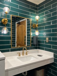 A bathroom with green subway tile walls, gold light