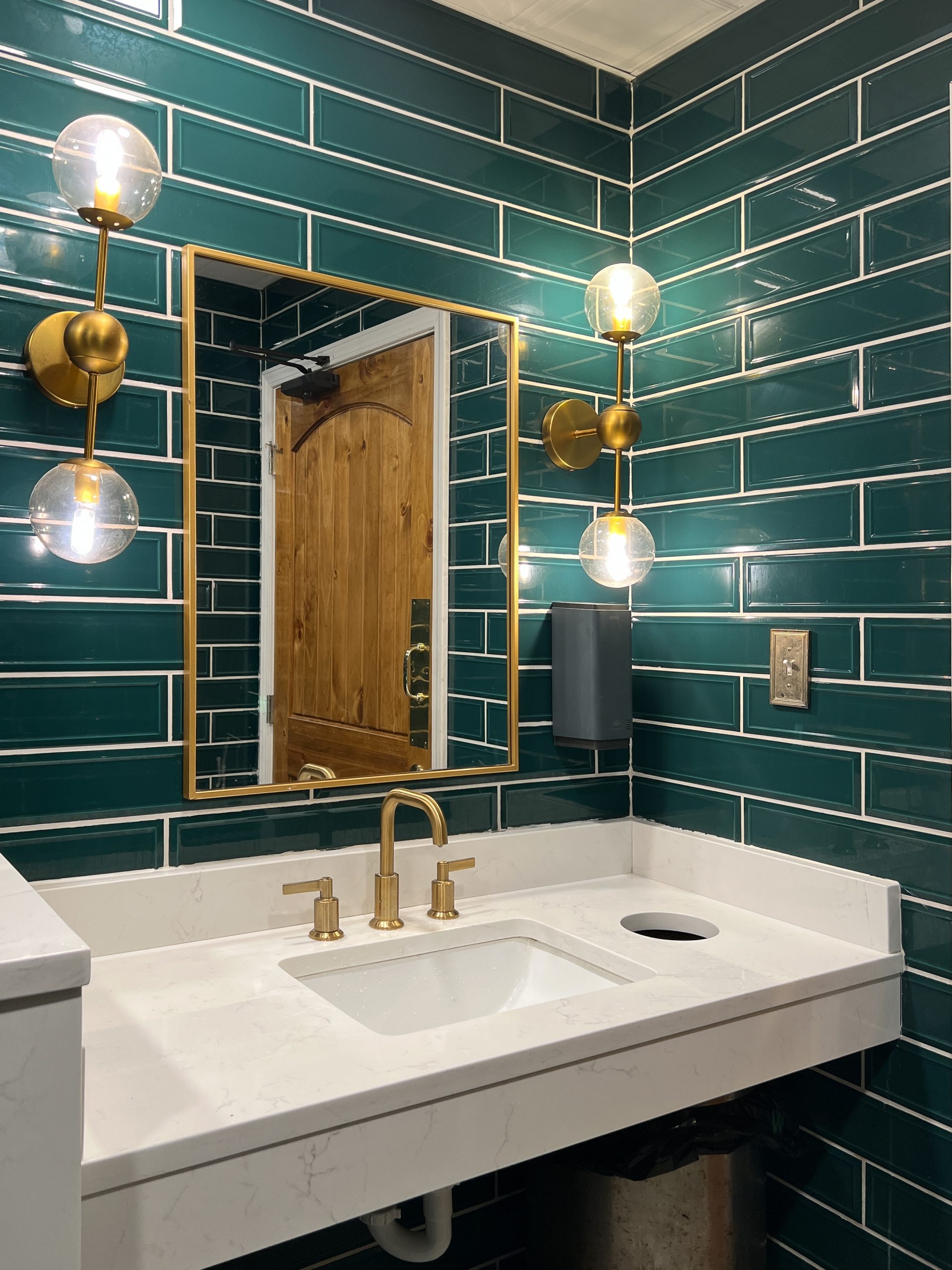 A bathroom with green subway tile walls, gold light